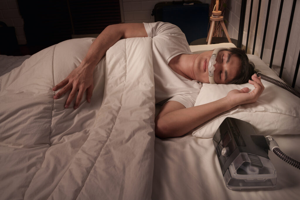 Peaceful Asian male asleep using CPAP mask and machine for obstructive sleep apnea and snoring remedy