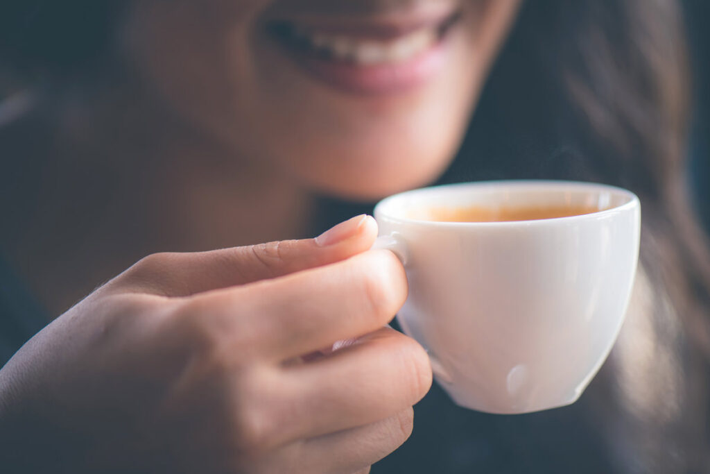 Smiling woman holing hot espresso coffee on hand at cafe in the morning